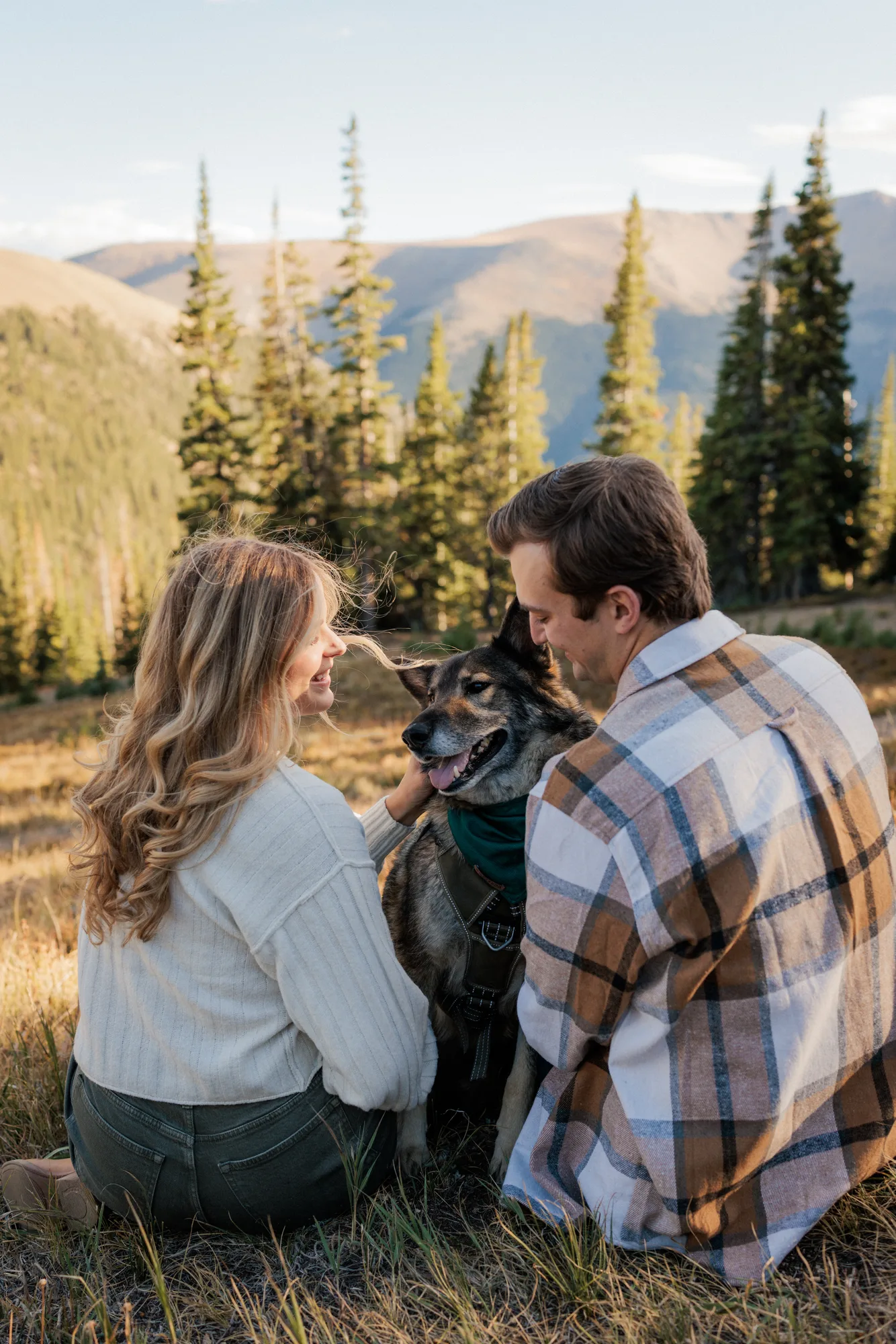 Jordan and Daelynn sitting in the grass with Churchill, facing the mountains