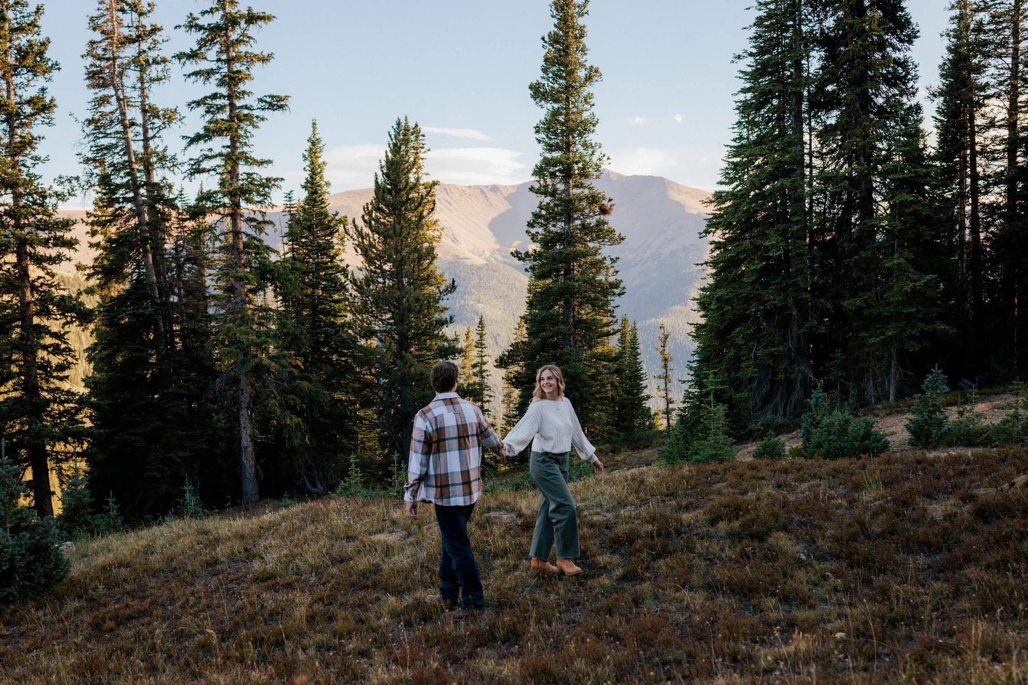 Jordan and Daelynn walking hand in hand through a mountain meadow